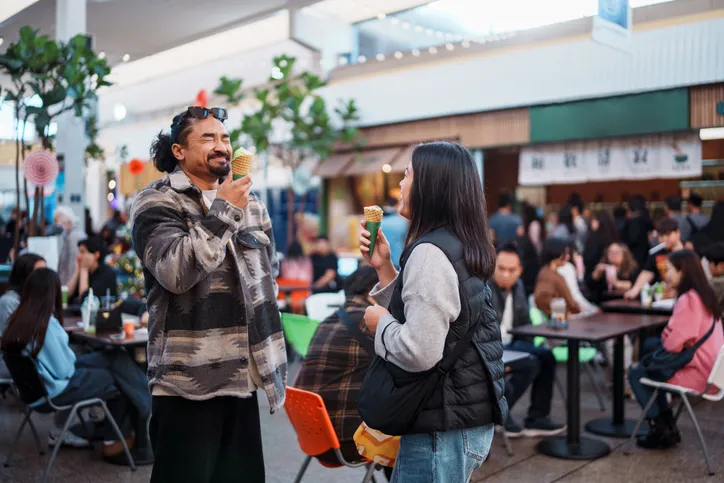 Two customers enjoying ice cream cones at a busy food hall