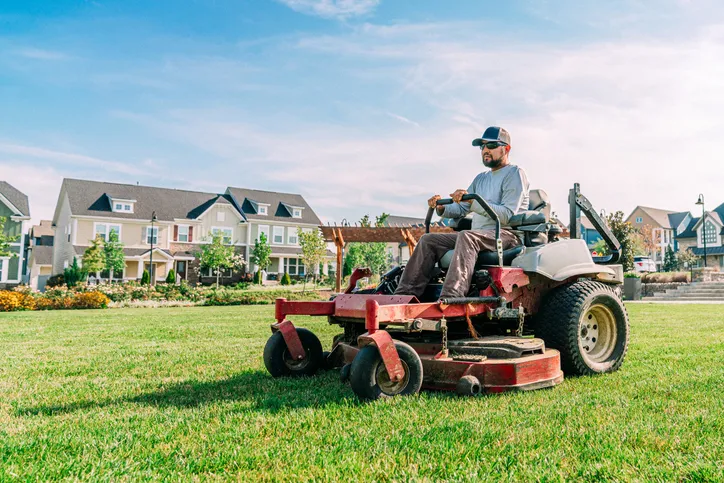 Landscaping crew member mowing a suburban lawn on a zero-turn mower