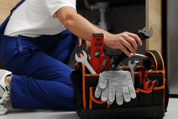 Plumber reaching for tools from a tool bag during an under-sink repair