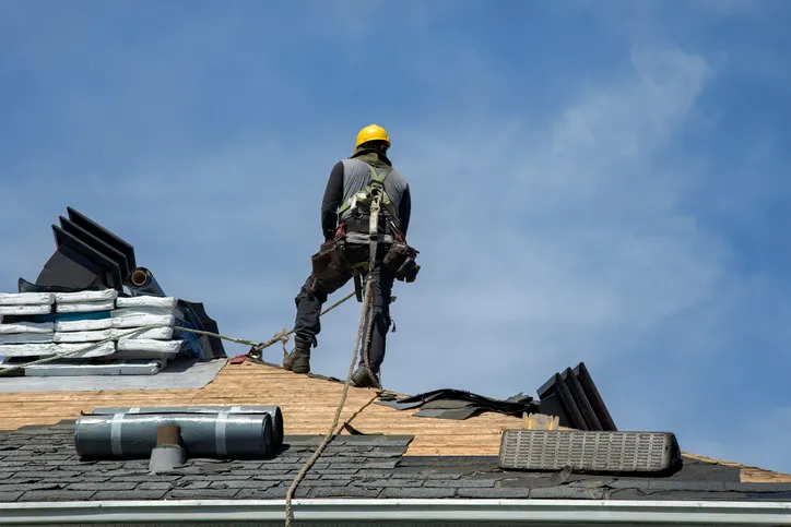 Roofing contractor in a safety harness working on a residential roof under a clear blue sky